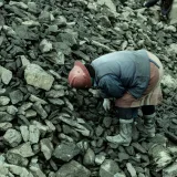 Un trabajador industrial con casco se inclina sobre un montón de piedras en una cantera.