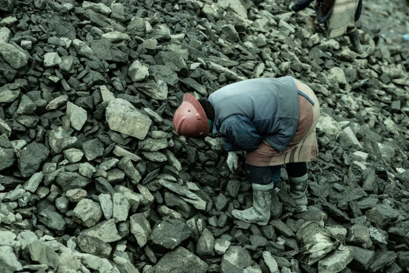 Un trabajador industrial con casco se inclina sobre un montón de piedras en una cantera.