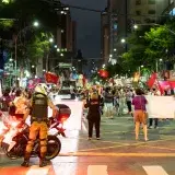 Vibrant urban protest scene at night with diverse crowd and police officer in foreground.