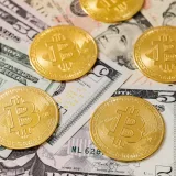Golden Bitcoin coins scattered over US dollar bills, symbolizing modern digital currency.