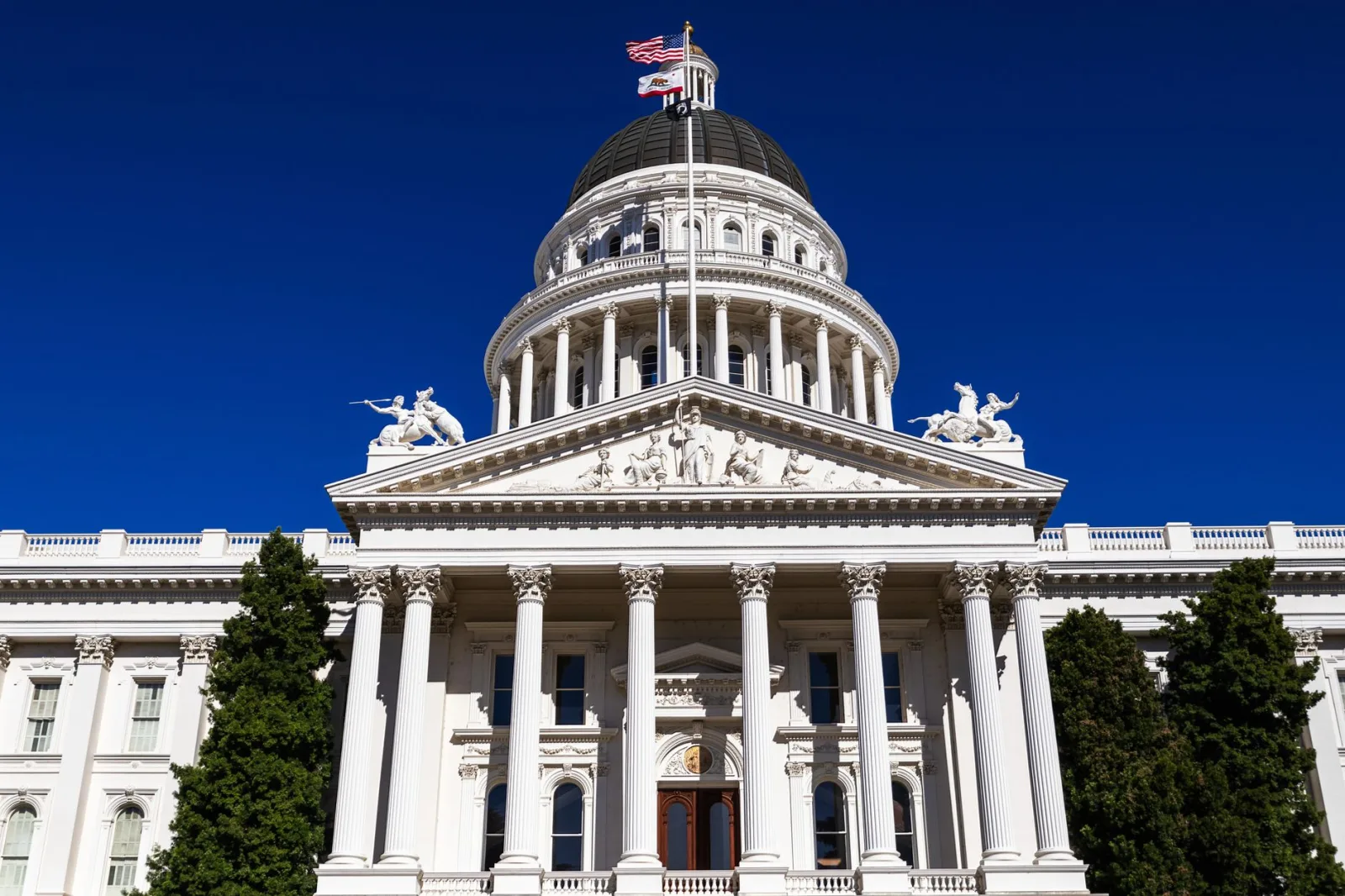 Vista del Capitolio del Estado de California bajo un cielo azul despejado e iluminado por el sol.