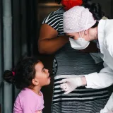 Un profesional de la salud examina a una niña pequeña en una clínica, acompañada por su madre.