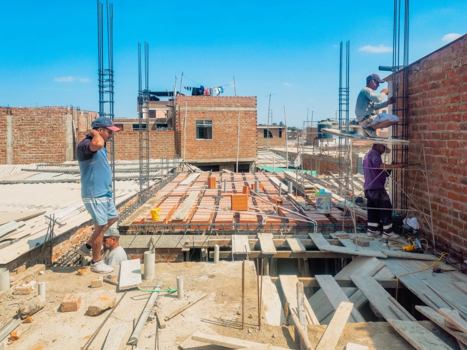 Obreros de la construcción levantan una estructura en Lambayeque, Perú, bajo un cielo azul despejado.
