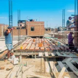 Obreros de la construcción levantan una estructura en Lambayeque, Perú, bajo un cielo azul despejado.
