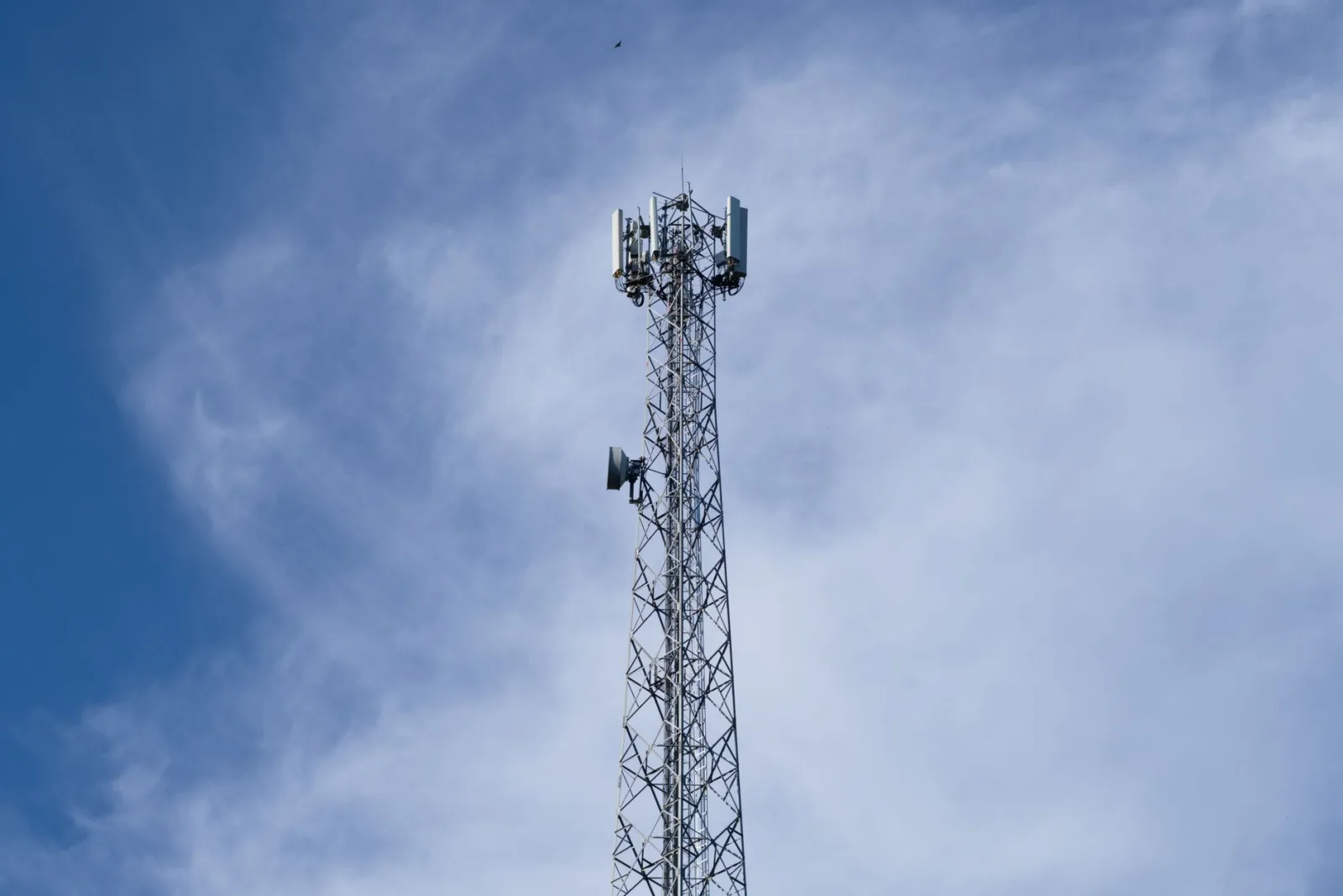 Una alta torre metálica de comunicaciones se alza frente a un cielo azul despejado con algunas nubes dispersas.