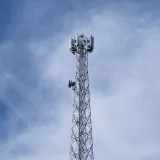 Una alta torre metálica de comunicaciones se alza frente a un cielo azul despejado con algunas nubes dispersas.