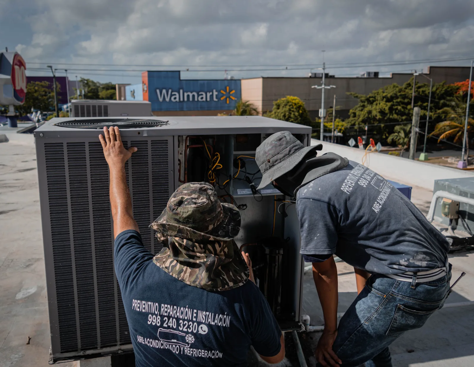 Dos técnicos reparan una unidad de HVAC en la azotea fuera de una tienda Walmart.