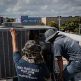 Dos técnicos reparan una unidad de HVAC en la azotea fuera de una tienda Walmart.