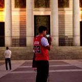 Hombre con camiseta de la selección de Jordania tomando una foto de un edificio histórico en Madrid al atardecer.