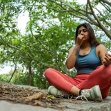Young woman meditating in a forest, practicing yoga breathing exercises on a stone platform.