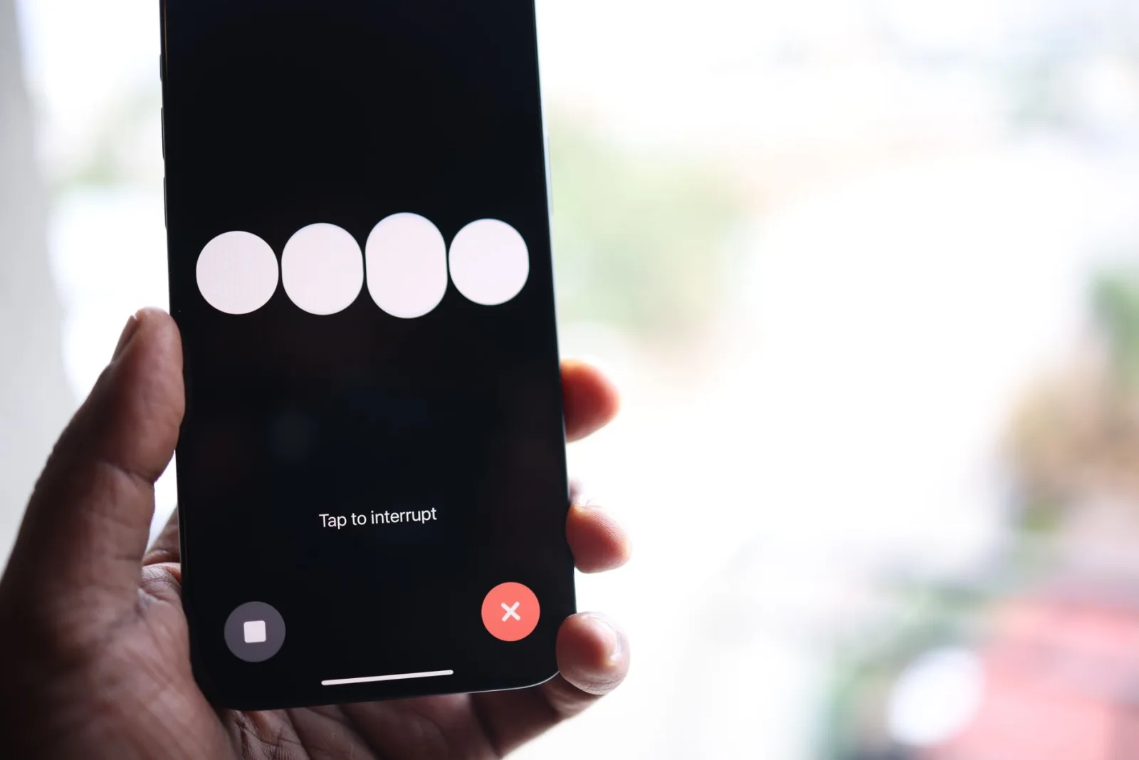 Primer plano de la pantalla de un teléfono inteligente que muestra el mensaje «Toca para interrumpir», sostenido en una mano.