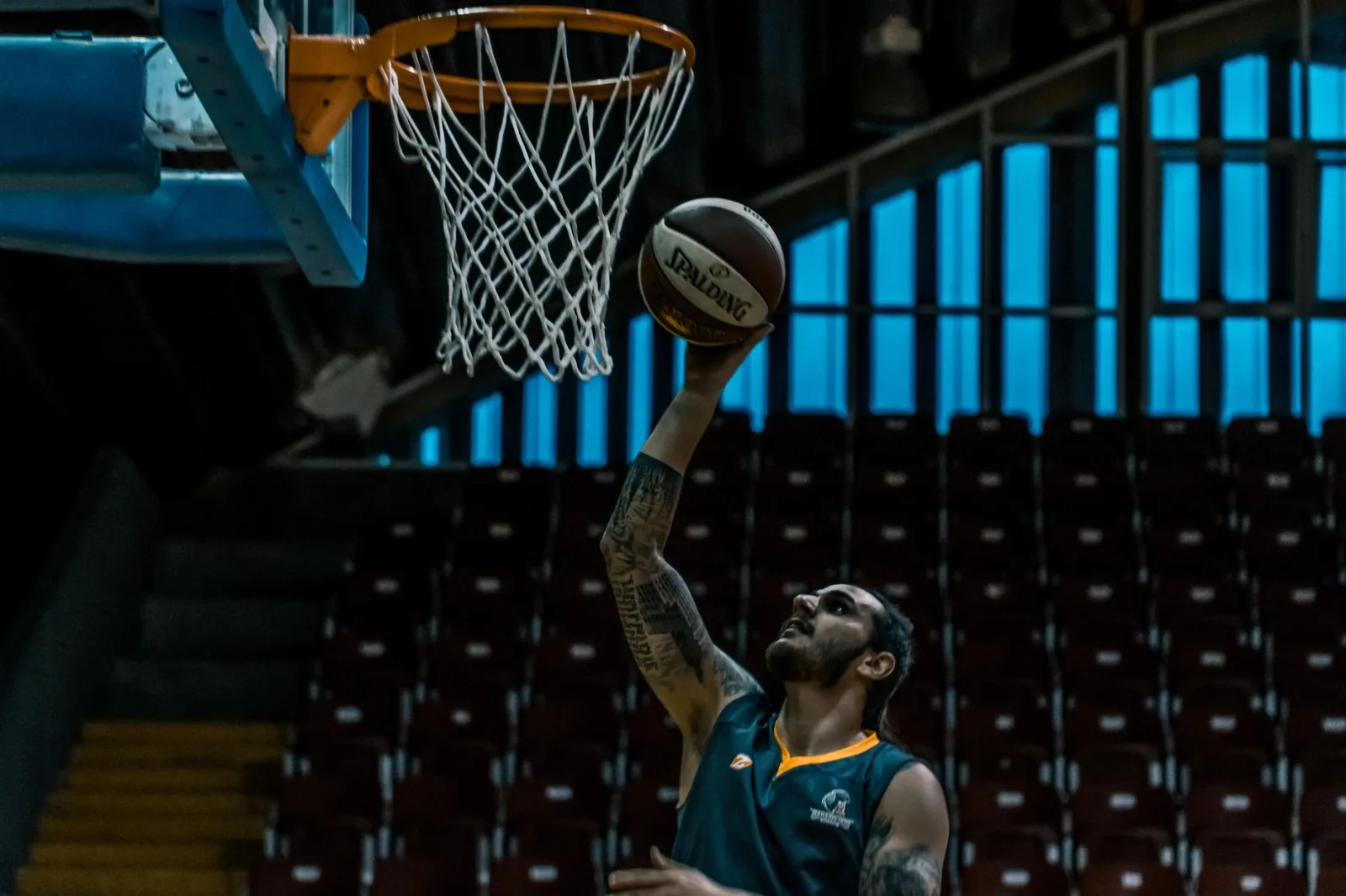 Un jugador de baloncesto concentrado anota en una cancha cubierta con poca iluminación, demostrando su talento atlético.