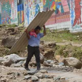 Un hombre camina con una lámina grande junto a una pared con un mural colorido en Mocoa, Colombia.