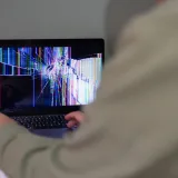 Una persona interactúa con una computadora portátil cuya pantalla está agrietada y distorsionada.