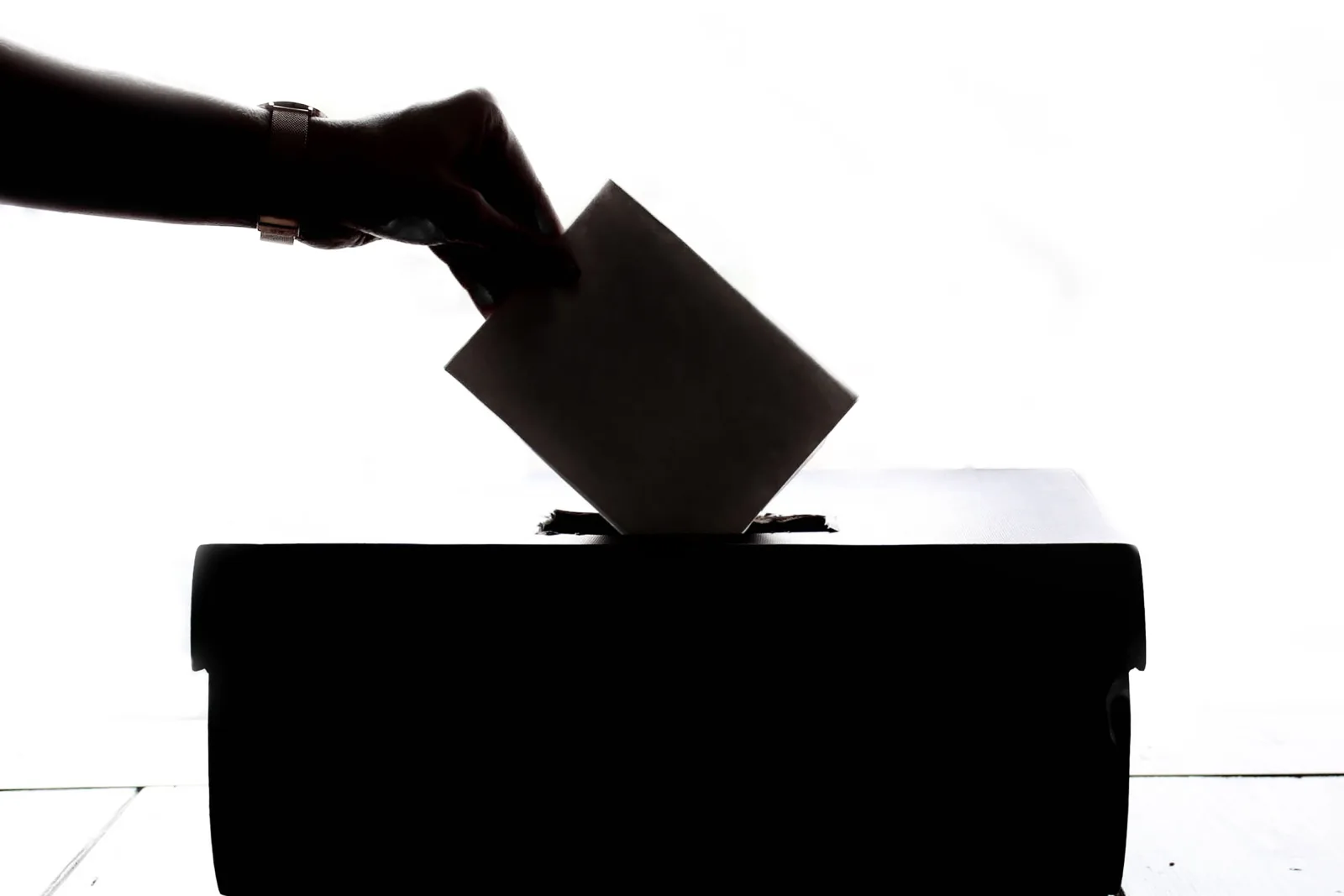 Silueta de una mano depositando un voto en una urna, símbolo de la democracia.