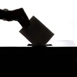 Silueta de una mano depositando un voto en una urna, símbolo de la democracia.