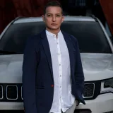 Stylish individual in blue blazer stands confidently by a white SUV. Rio de Janeiro, Brasil.
