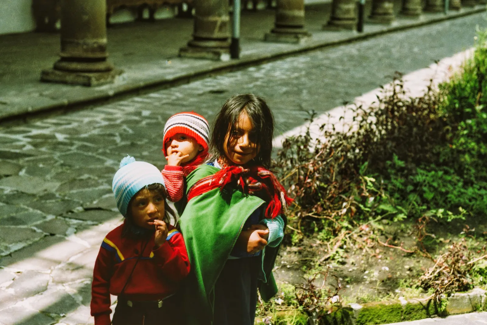 Tres niños con ropa tradicional en una calle empedrada de Ecuador.