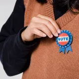 Persona con una insignia que dice «Vota», símbolo de la participación en la democracia y las elecciones.