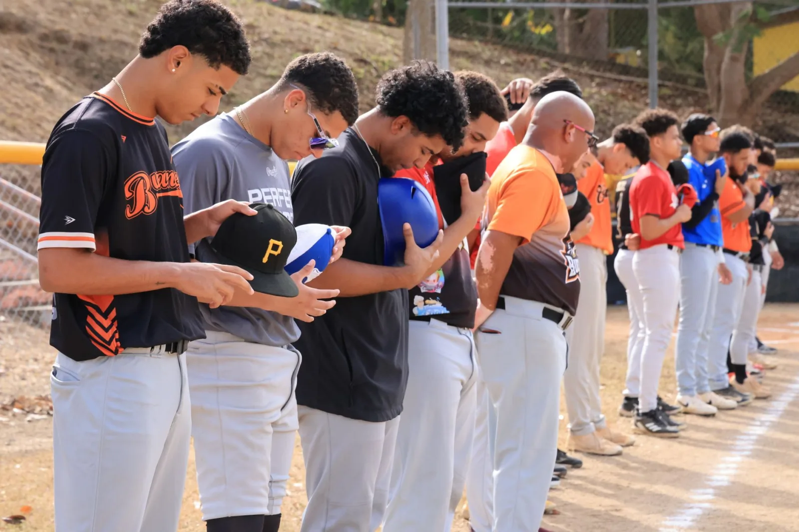 Jugadores de béisbol en fila con las gorras quitadas durante la ceremonia del himno nacional antes del partido, al aire libre.