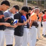 Jugadores de béisbol en fila con las gorras quitadas durante la ceremonia del himno nacional antes del partido, al aire libre.