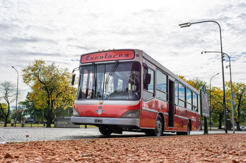 Autobús escolar vintage rojo estacionado en una calle de Buenos Aires en un otoño soleado.