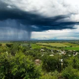 Dark storm clouds and heavy rain over lush green fields, creating a dramatic landscape scene.