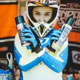 Piloto de motocross con equipo completo sosteniendo latas de spray lubricante que promocionan Liqui Moly.