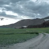 Aerial drones hovering over a picturesque landscape with fields and mountains under a cloudy sky.