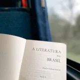 An open book titled 'A Literatura no Brasil' by a window, offering a serene travel experience.