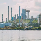 A large industrial refinery complex with tall chimneys by the waterfront under a clear sky.