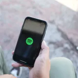 Close-up of a hand holding a smartphone displaying the Spotify app, outdoors.