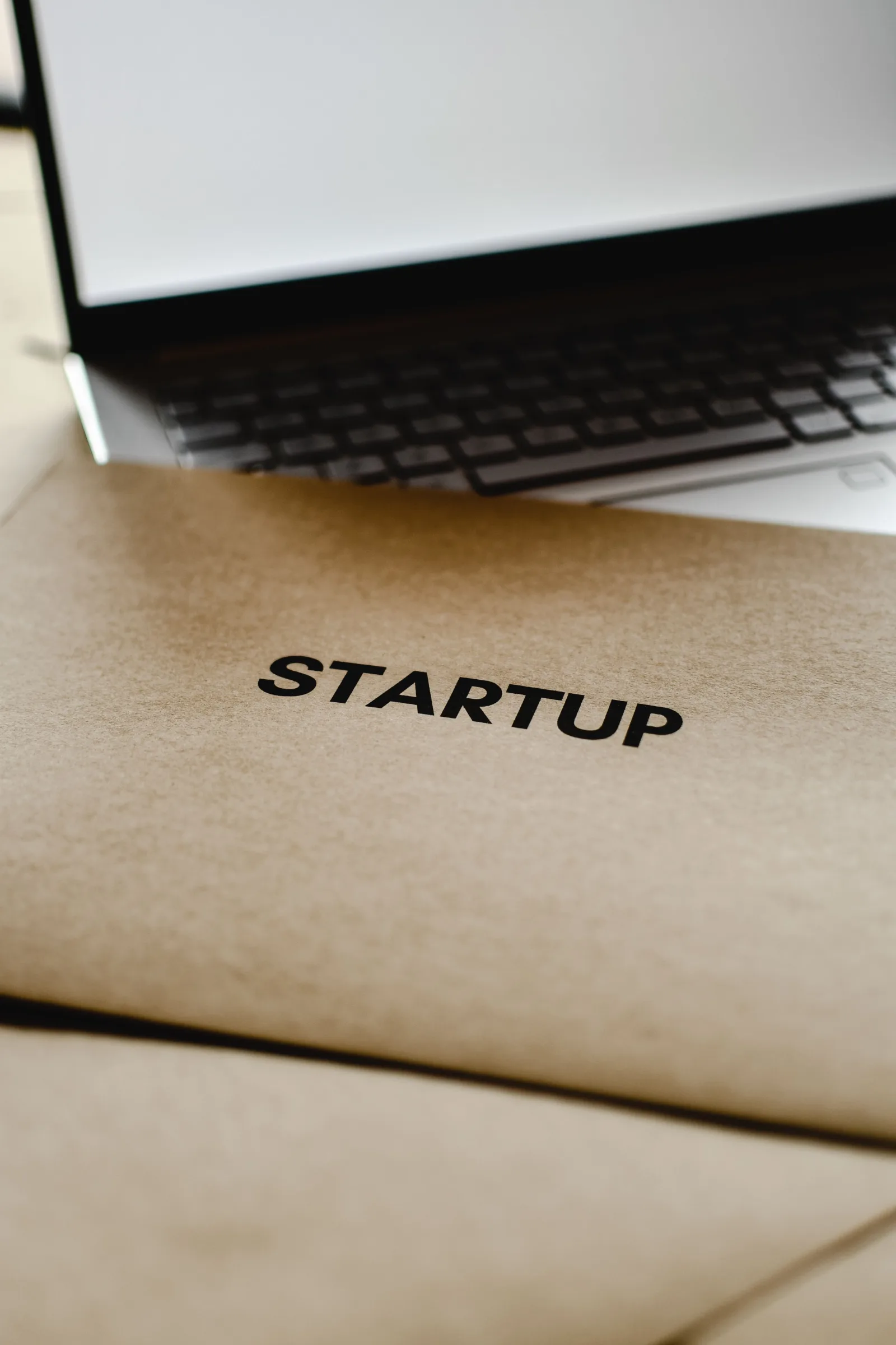 Primer plano de una carpeta de inicio y una computadora portátil, que representan la innovación empresarial y tecnológica.