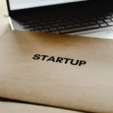 Primer plano de una carpeta de inicio y una computadora portátil, que representan la innovación empresarial y tecnológica.