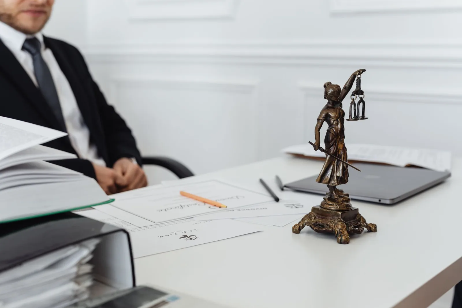 Espacio de trabajo de un profesional legal con una estatua de la Justicia, documentos y un portátil.
