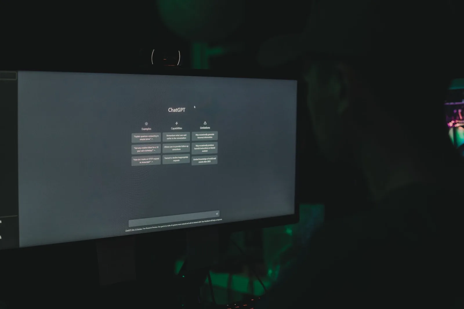 Una persona interactúa con la interfaz de ChatGPT en la pantalla de una computadora, en una habitación con poca iluminación.