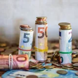 Primer plano de billetes de euro enrollados y monedas sobre una mesa, como símbolo de las finanzas y el ahorro.