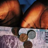 Primer plano de unas manos que sostienen monedas de distintos valores y un billete, en alusión a la gestión financiera.