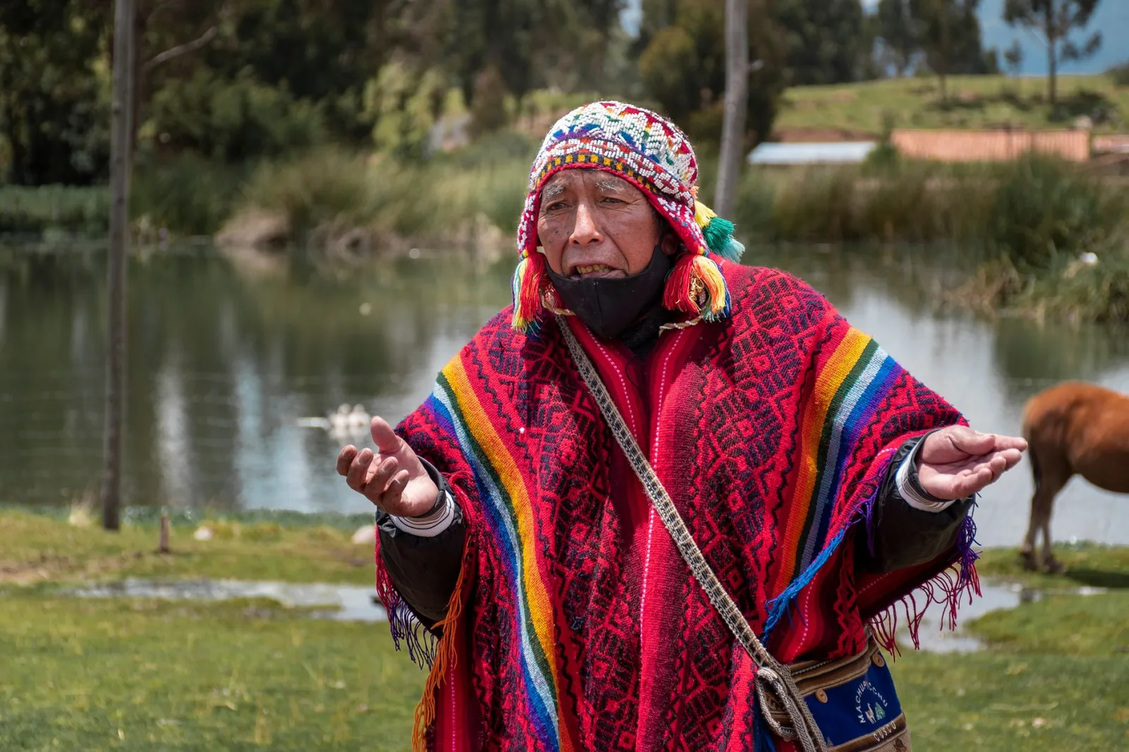 Un hombre mayor vestido con ropa tradicional peruana de colores vivos cerca de un lago pintoresco en Cusco, Perú.
