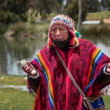 Un hombre mayor vestido con ropa tradicional peruana de colores vivos cerca de un lago pintoresco en Cusco, Perú.
