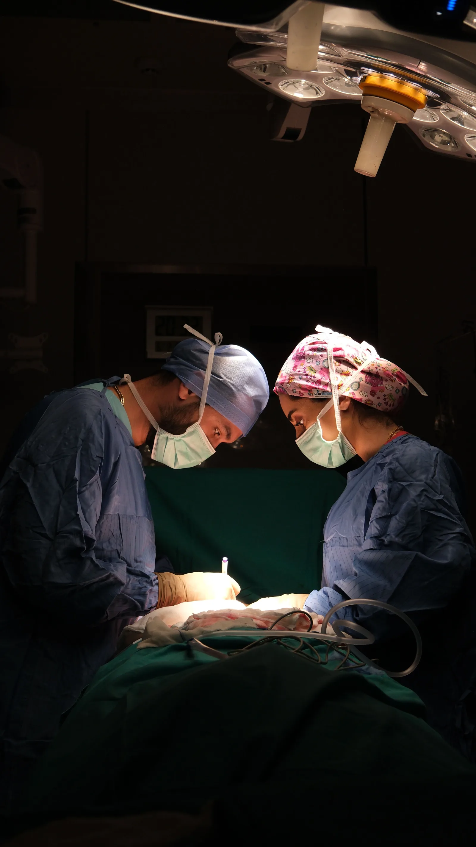 Cirujanos concentrados operando bajo una iluminación dramática en un quirófano de hospital.