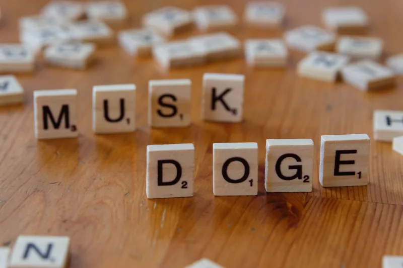 Fichas de Scrabble formando las palabras 'DOGE' y 'MUSK' sobre una mesa de madera, destacando la cultura de internet y las criptomonedas.