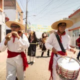 Desfile tradicional en México con músicos vestidos con atuendos culturales y coloridas decoraciones callejeras.