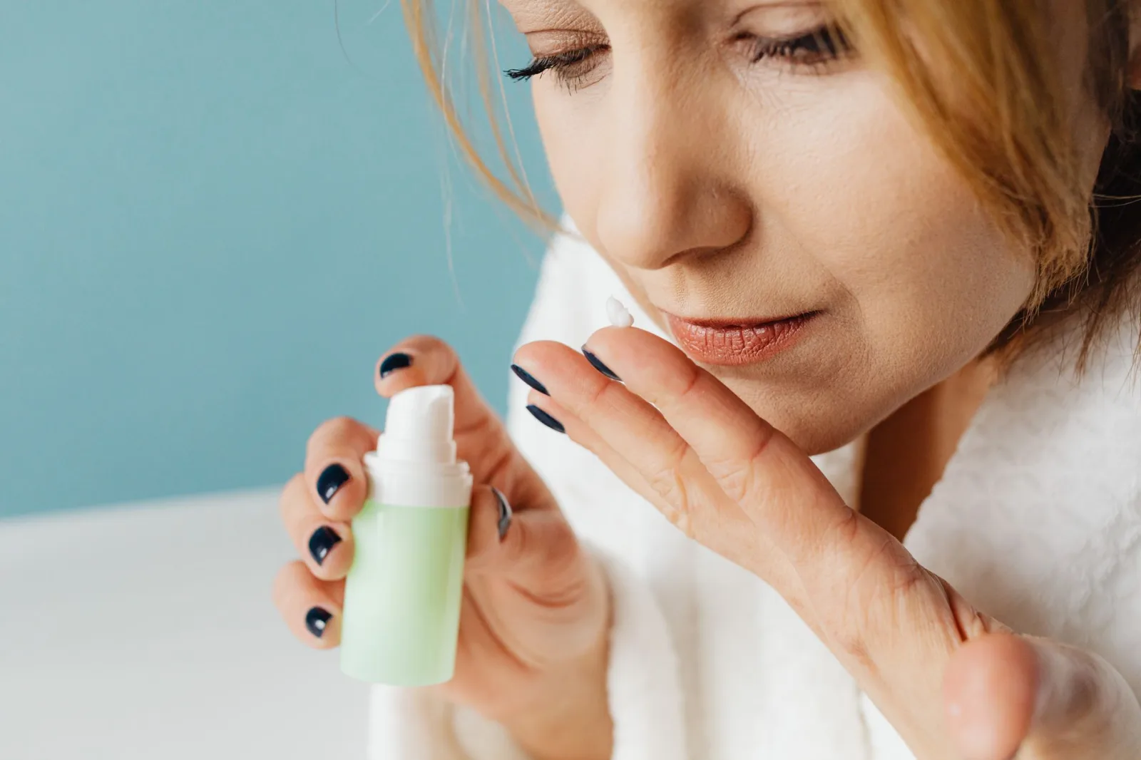 Primer plano de una mujer en bata aplicándose crema para el cuidado de la piel, centrada en su rutina de autocuidado y belleza.