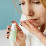 Primer plano de una mujer en bata aplicándose crema para el cuidado de la piel, centrada en su rutina de autocuidado y belleza.