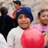 Cheerful children playing outdoors in San Juan de Lurigancho, Peru, holding red balloons and smiling.