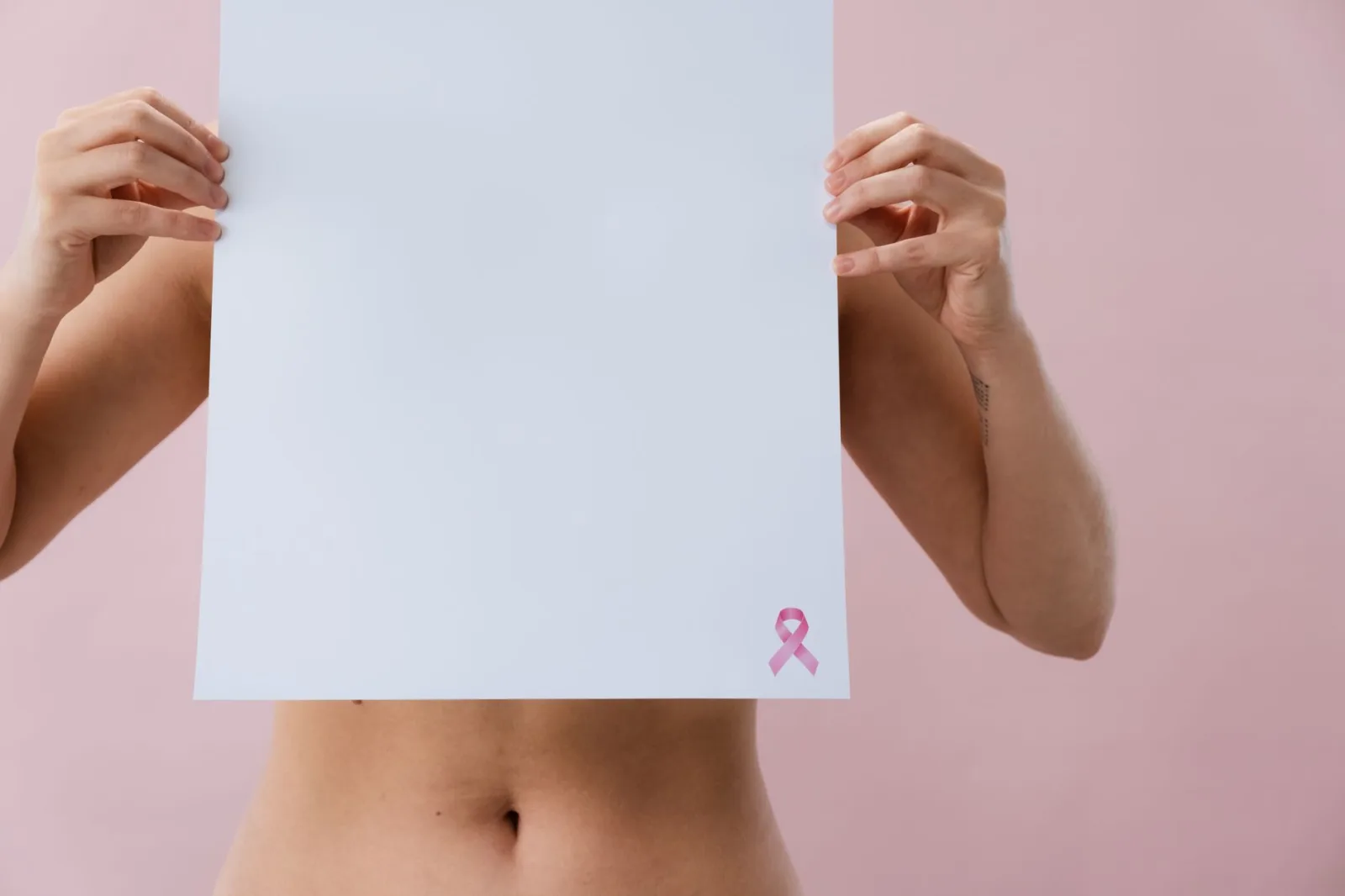 Imagen de una mujer sosteniendo una hoja en blanco con un lazo rosa para crear conciencia sobre el cáncer de mama.