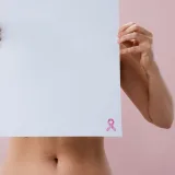 Imagen de una mujer sosteniendo una hoja en blanco con un lazo rosa para crear conciencia sobre el cáncer de mama.