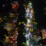 Vista aérea de una animada calle urbana por la noche, con tráfico iluminado y vías bordeadas de árboles.