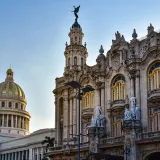 View of the National Capitol Building and Grand Theater in Havana, Cuba against a blue sky.